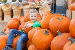 little excited kid enjoying time at pumpkin patch sitting in the huge pile of pumpkins